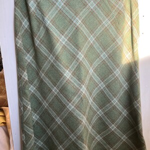 Puede incluir: Una falda de cuadros verdes con un patr&oacute;n de cuadros blancos y marrones. La falda es de largo hasta la rodilla y tiene una silueta recta.