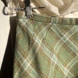 Puede incluir: Una falda de cuadros verdes con un patr&oacute;n de cuadros marrones y blancos. La falda est&aacute; hecha de una tela suave y tejida.