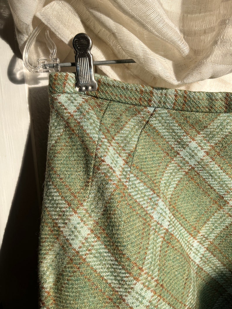 Puede incluir: Una falda de cuadros verdes con un patr&oacute;n de cuadros marrones y blancos. La falda est&aacute; hecha de una tela suave y tejida.