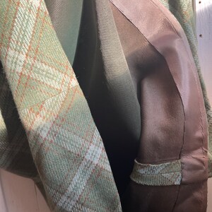 Puede incluir: Primer plano del interior de una chaqueta de cuadros verdes con forro marr&oacute;n. El forro est&aacute; cosido con una costura curva.