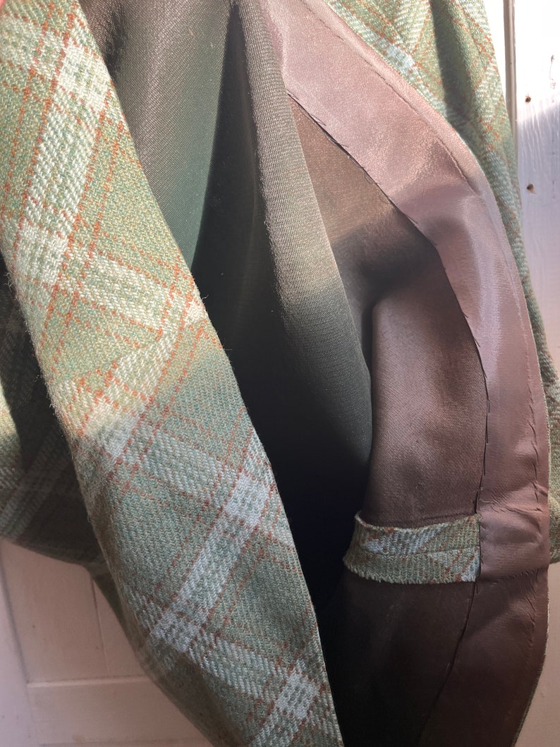 Puede incluir: Primer plano del interior de una chaqueta de cuadros verdes con forro marr&oacute;n. El forro est&aacute; cosido con una costura curva.