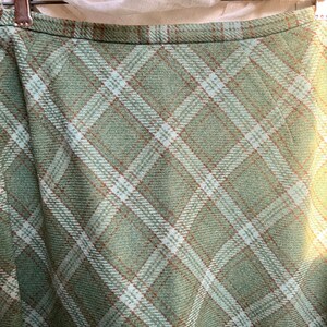 Puede incluir: Una falda de cuadros verdes con rayas blancas y marrones. La falda est&aacute; hecha de una tela suave y tejida.