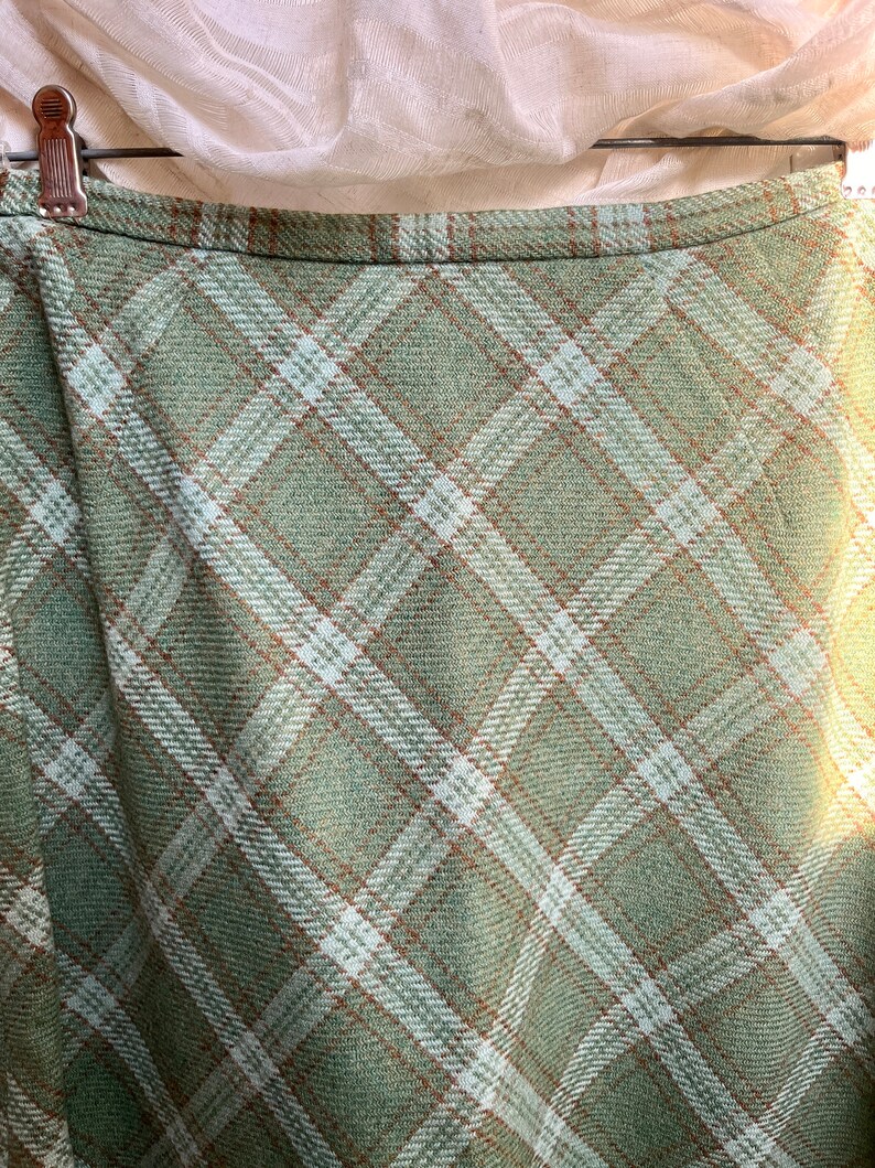 Puede incluir: Una falda de cuadros verdes con rayas blancas y marrones. La falda est&aacute; hecha de una tela suave y tejida.