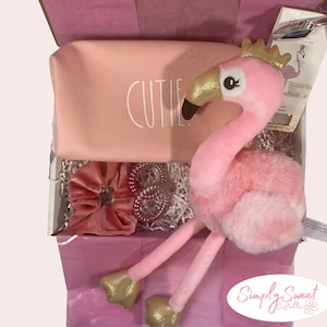 May include: Pink gift box filled with a pink flamingo plush toy, a pink and white makeup bag with the word "CUTIE" printed on it, a pink velvet hair scrunchie, and a pink beaded bracelet. The box is lined with pink tissue paper.