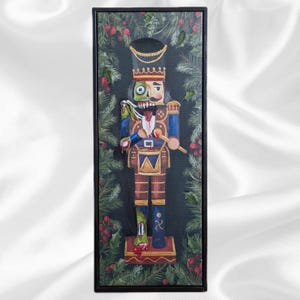 May include: A framed painting of a zombie nutcracker soldier. The nutcracker is painted in blue, brown, and gold, with a green and red color scheme. The background is black with green leaves and red berries.