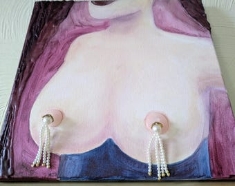 May include: A rectangular canvas painting depicting a stylized torso in shades of pale pink, framed by deep purple and blue painted areas. Two circular pink accents are attached to the chest, each featuring dangling white pearl-like beaded tassels.