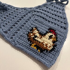 May include: A blue crocheted face mask with a brown, white, and red embroidered chicken design.