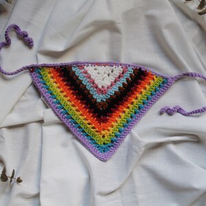 Könnte beinhalten: Ein bunter, gehäkelter Dreiecksschal mit einem Regenbogenmuster und lila Bändern.