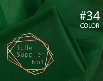 Może przedstawiać: Zbliżenie na ciemnozielony tiul. Tkanina jest złożona i udrapowana, co ukazuje jej fakturę. Tekst "Tulle Supplier No1" znajduje się w złotej geometrycznej ramce. Tekst "#34 COLOR" jest w białym kolorze.