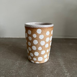 May include: A brown ceramic mug with a white polka dot pattern. The mug has a speckled glaze and a white rim.
