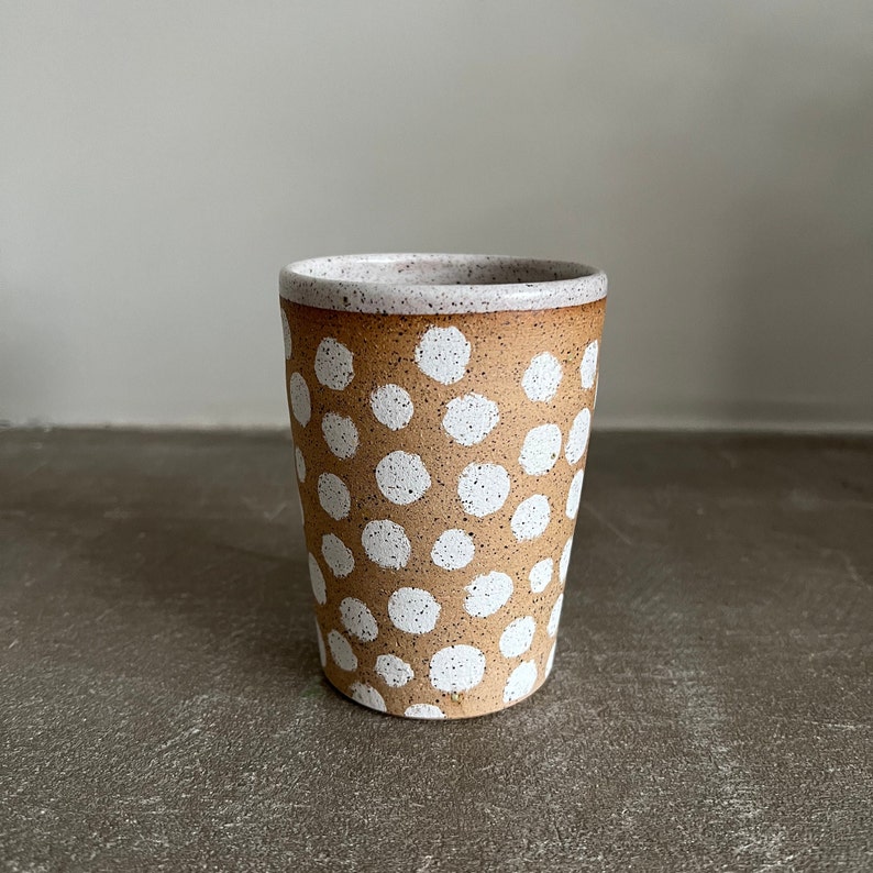 May include: A brown ceramic mug with a white polka dot pattern. The mug has a speckled glaze and a white rim.