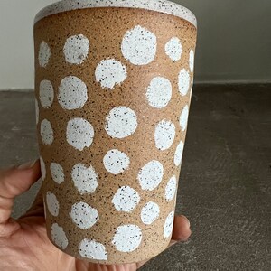 May include: A brown ceramic mug with white polka dots. The mug has a speckled texture.