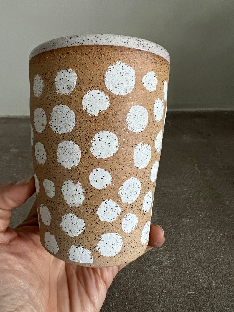 May include: A brown ceramic mug with white polka dots. The mug has a speckled texture.