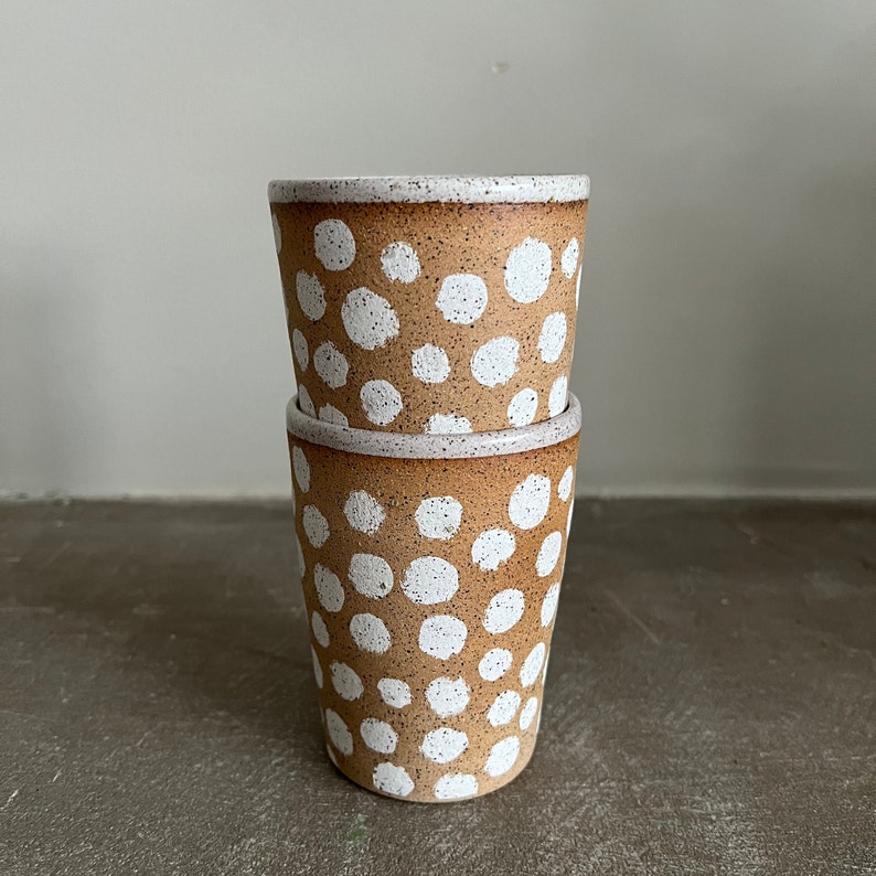 May include: Two brown ceramic mugs with white polka dots. The mugs are stacked on top of each other.