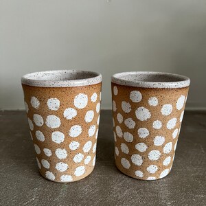 May include: Two ceramic mugs with a speckled brown glaze and white polka dots.