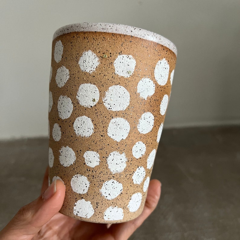 May include: A brown ceramic mug with white polka dots. The mug has a speckled brown glaze and a white rim.