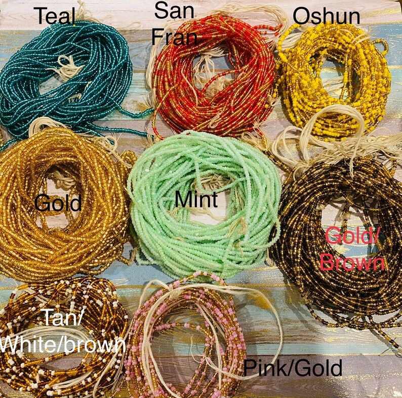 May include: Assortment of colourful beaded waist beads in various colours, including teal, gold, mint, pink, and brown. The beads are arranged in a circle on a wooden surface. The text "Teal", "San Fran", "Oshun", "Gold", "Mint", "Goldy Brown", "Tan/White/Brown", and "Pink/Gold" are written on the image.