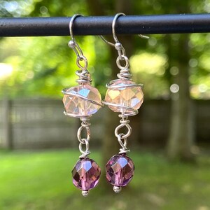 May include: A pair of silver dangle earrings with a pink iridescent crystal bead and a smaller purple crystal bead on each earring.