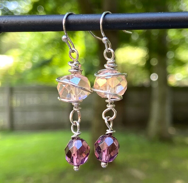 May include: A pair of silver dangle earrings with a pink iridescent crystal bead and a smaller purple crystal bead on each earring.
