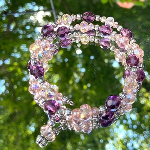 May include: A multi-strand bracelet with pink and purple crystal beads. The bracelet is made with silver-toned metal beads and has a clasp closure.