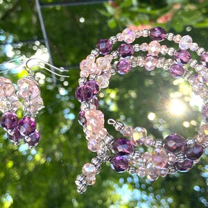 May include: A set of purple and pink crystal earrings and a matching bracelet. The earrings are dangle style and the bracelet is a wrap style.