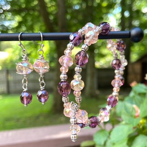 May include: A set of jewelry featuring a pair of iridescent pink and purple dangle earrings and a double-strand bracelet with iridescent pink and purple beads.
