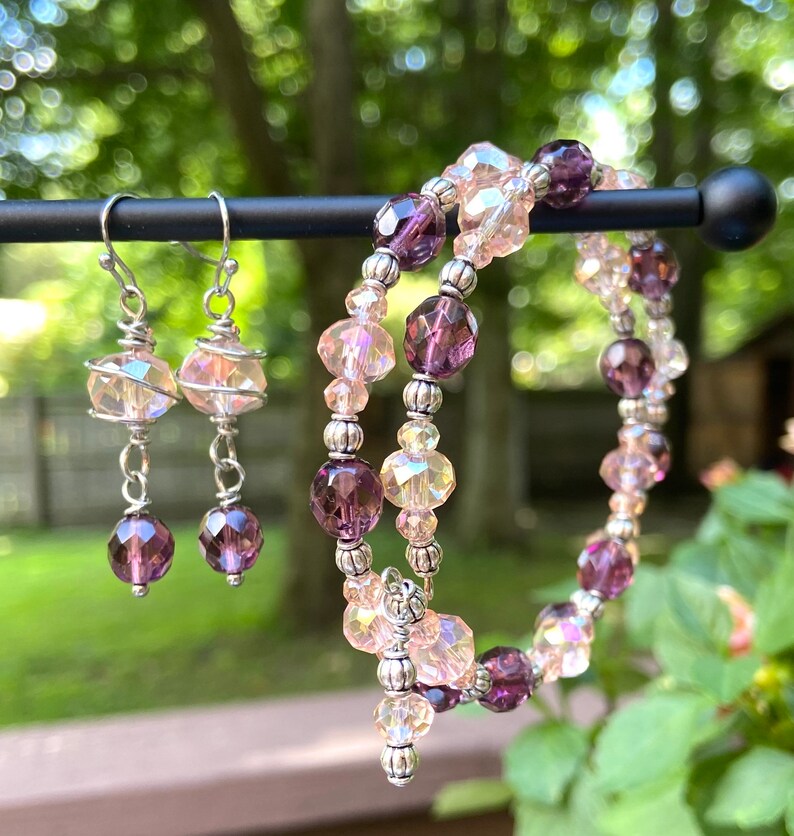 May include: A set of jewelry featuring a pair of iridescent pink and purple dangle earrings and a double-strand bracelet with iridescent pink and purple beads.
