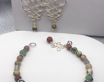 May include: A jewelry set featuring earrings and a bracelet. The earrings have a silver wire design with a swirl pattern, and are adorned with peach and green beads. The bracelet has a variety of colorful beads, including pink, green, and iridescent beads.