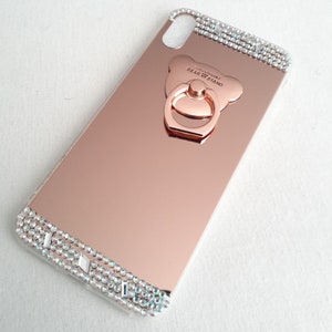 May include: Rose gold mirror phone case with a clear, sparkly, rhinestone trim and a rose gold bear-shaped ring holder with the text "FASHION BEAR STAND".