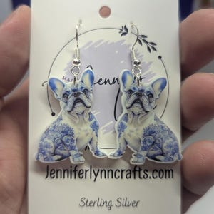 Op de afbeelding: Een paar sterling zilveren oorbellen met een Frans bulldog ontwerp. De bulldog is wit met blauwe en witte bloemenpatronen. De oorbellen zijn op een witte kaart met de tekst "Jenniferlynncrafts.com" en "Sterling zilver".
