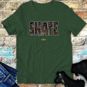 Può includere: Una maglietta verde con la parola "SKATE" scritta in nero con varie parole relative allo skateboard all'interno delle lettere. Le parole sono di diversi colori, tra cui rosso, arancione, giallo e marrone.
