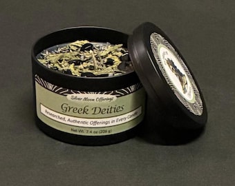 May include: A black candle tin with the lid slightly ajar, revealing a candle with dried herbs and crystals. The label reads "Greek Deities" and "Net Wt. 7.4 oz (209 g)." The lid features a decorative design.
