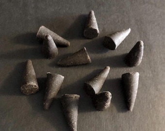 May include: A selection of dark brown incense cones, each with a conical shape and textured surface, displayed on a dark background. The arrangement suggests use in aromatherapy or spiritual practices.