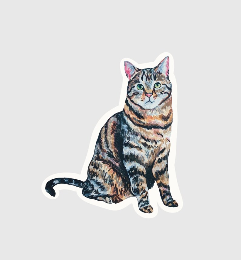 May include: A sticker featuring a watercolor illustration of a tabby cat in a seated position. The cat has brown and black stripes, green eyes, and pink inner ears. The sticker is cut around the cat's outline.