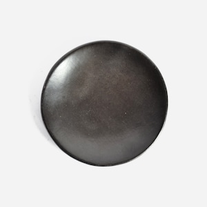 May include: A black ceramic plate with a slightly rounded edge. The plate is smooth and has a matte finish.