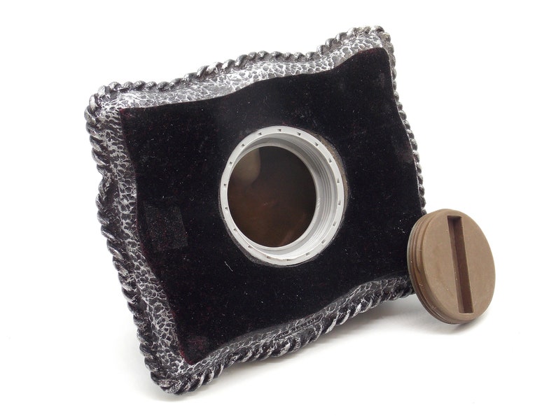 May include: A black velvet cremation urn with a silver rope design around the edge. The urn has a round opening on the top with a brown lid.