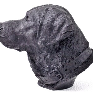 Puede incluir: Escultura de cabeza de perro Labrador Retriever negro. La escultura est&aacute; hecha de un material gris oscuro y tiene un aspecto realista. El perro lleva un collar de cuero negro con una hebilla.