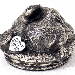 K&ouml;nnte beinhalten: Silberne Katzenurne aus Metall mit einem herzf&ouml;rmigen Anh&auml;nger mit der Aufschrift "KITTY Beloved Mama 2007-2018".