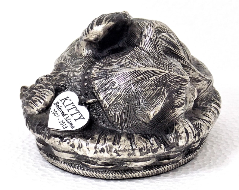 K&ouml;nnte beinhalten: Silberne Katzenurne aus Metall mit einem herzf&ouml;rmigen Anh&auml;nger mit der Aufschrift "KITTY Beloved Mama 2007-2018".