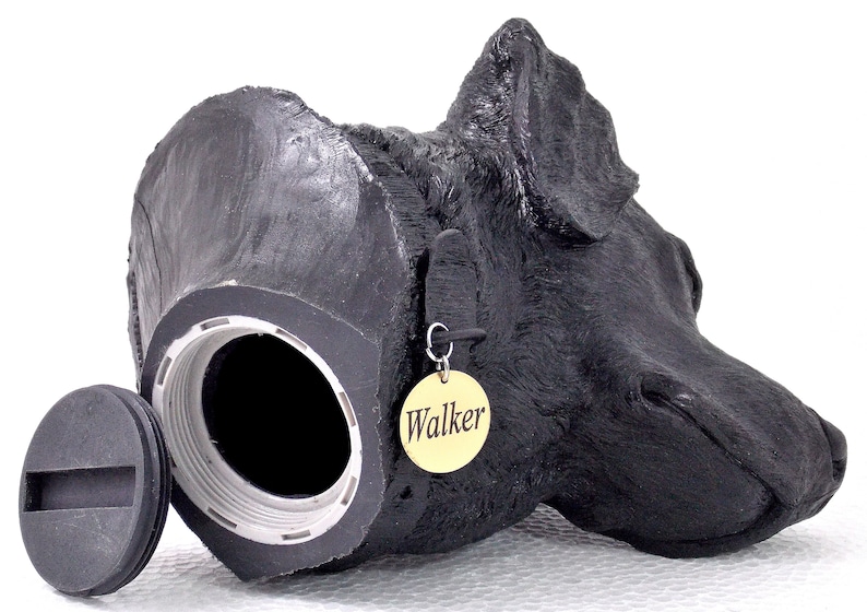 May include: Black dog head pet urn with a removable lid and a gold tag that says "Walker".