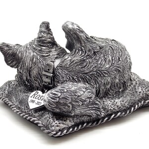 May include: Silver memorial figurine of a dog lying on a pillow with a heart-shaped tag that reads "Rosie 1998-2021".