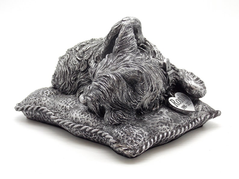 May include: Silver pet memorial figurine of a sleeping dog on a pillow with a heart-shaped tag that reads "Rosie 1991-2017".
