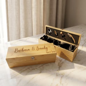 May include: Two bamboo wine boxes, one closed and one open, displaying wine tools. The closed box is engraved with "Barbara & Sandy" and "April 4, 2026." The open box reveals a black satin interior and various wine accessories.