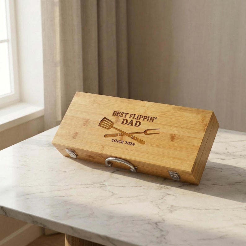 May include: A rectangular bamboo grilling tool box with the text "BEST FLIPPIN' DAD SINCE 2024" and crossed spatula and fork design. The box has a silver handle and latches.
