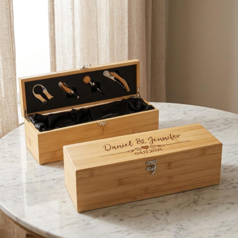 May include: Two bamboo wine boxes, one open to reveal wine tools and a black satin lining. The closed box has the names "Daniel & Jennifer" and the date "04.17.2021" engraved on the lid. The boxes are on a marble surface.