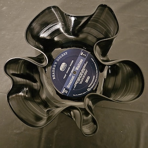 May include: A decorative bowl crafted from a repurposed vinyl record. The bowl is black with a wavy, petal-like design. The record label in the center reads "Reader's Digest" and "Greatest Waltzes."