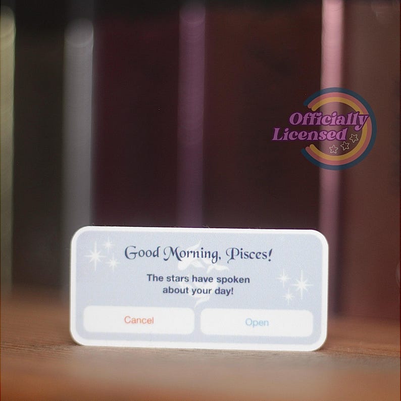 May include: A white rectangular card with rounded corners displays the text "Good Morning, Pisces!" and "The stars have spoken about your day!" with "Cancel" and "Open" buttons. The card is officially licensed.