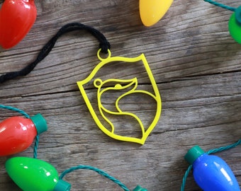 May include: Yellow Christmas ornament shaped like a shield with a badger silhouette inside. The ornament is hanging from a black string and is surrounded by colorful Christmas lights.