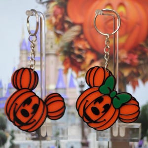 May include: Two orange pumpkin-shaped Mickey Mouse and Minnie Mouse keychains with black outlines. Minnie Mouse has a green bow.