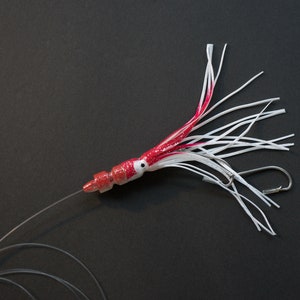 May include: A red and white squid lure with a long, thin body and a hook at the end. The lure is attached to a clear fishing line.